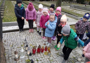 Dzieci zapalają znicze na grobach żołnierzy i ofiar poległych w obronie ojczyzny