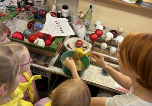 Dzieci zwiedzają fabrykę bombek i poznają kolejne etapy powstawnia tych ozdób świątecznych