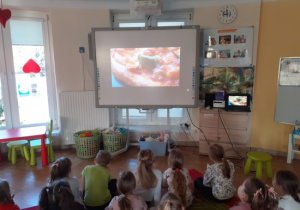 Dzieci oglądają film edukacyjny nt. historii powstania pizzy.