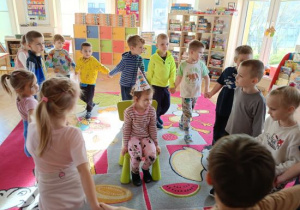 Dzieci tańczą w kole i śpiewają koleżance 100 lat.