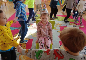 Dzieci tańczą w kole i śpiewają koleżance 100 lat.