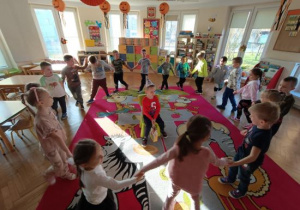 Dzieci tańczą w kole i śpiewają koledze 100 lat.