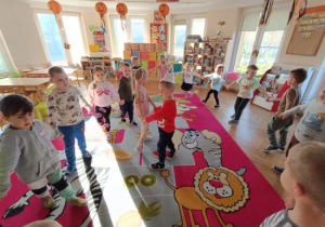 Dzieci tańczą w kole i śpiewają koledze 100 lat.