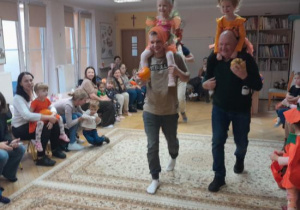 Rodzice i dzieci uczestniczą w zabawach ruchowych z dynią.