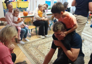 Rodzice i dzieci uczestniczą w zabawach ruchowych z dynią.