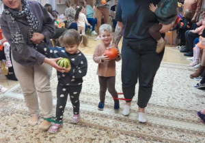 Rodzice i dzieci uczestniczą w zabawach ruchowych z dynią.