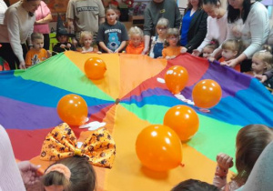 Rodzice i dzieci uczestniczą w zabawach ruchowych z dynią.