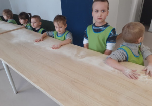 Dzieci stoją przy stołach.