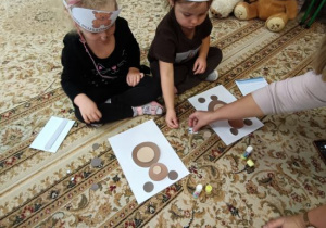 Dzieci biorą udział w zadaniu: wyklejanie misia wg wzoru.