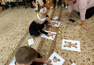 Dzieci biorą udział w zadaniu: wyklejanie misia wg wzoru.
