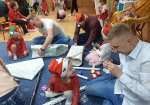 Dzieci i rodzice biorą udział w spotkaniu mikołajkowym.