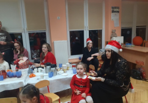 Dzieci i rodzice biorą udział w spotkaniu mikołajkowym.